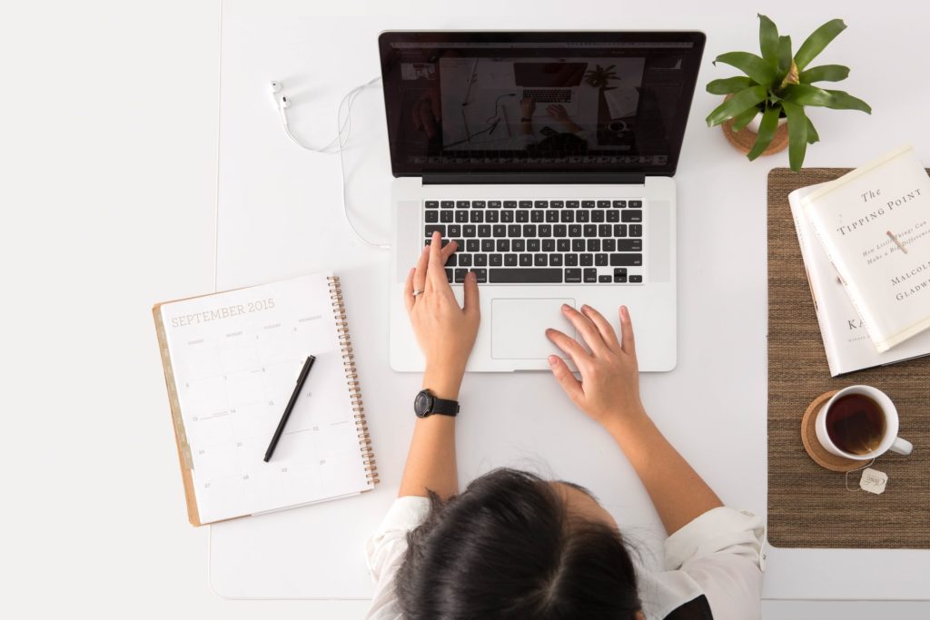 Woman sitting at table with fingers on laptop and notebook and pen next to her