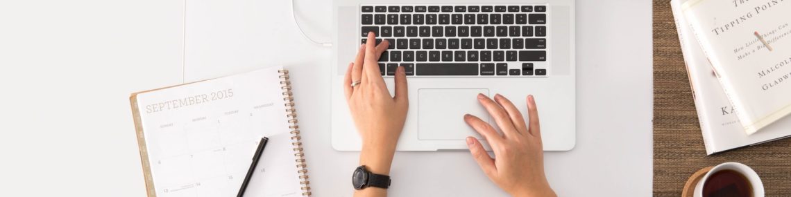 Woman sitting at table with fingers on laptop and notebook and pen next to her